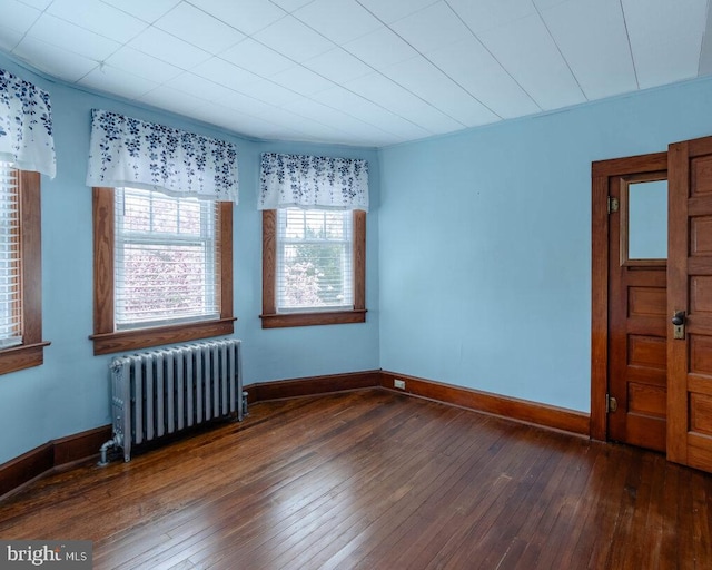 empty room with wood-type flooring, baseboards, and radiator heating unit