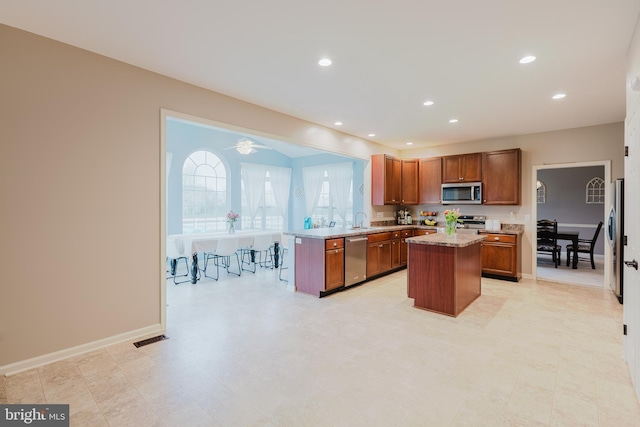 kitchen with brown cabinets, appliances with stainless steel finishes, a sink, a center island, and a peninsula