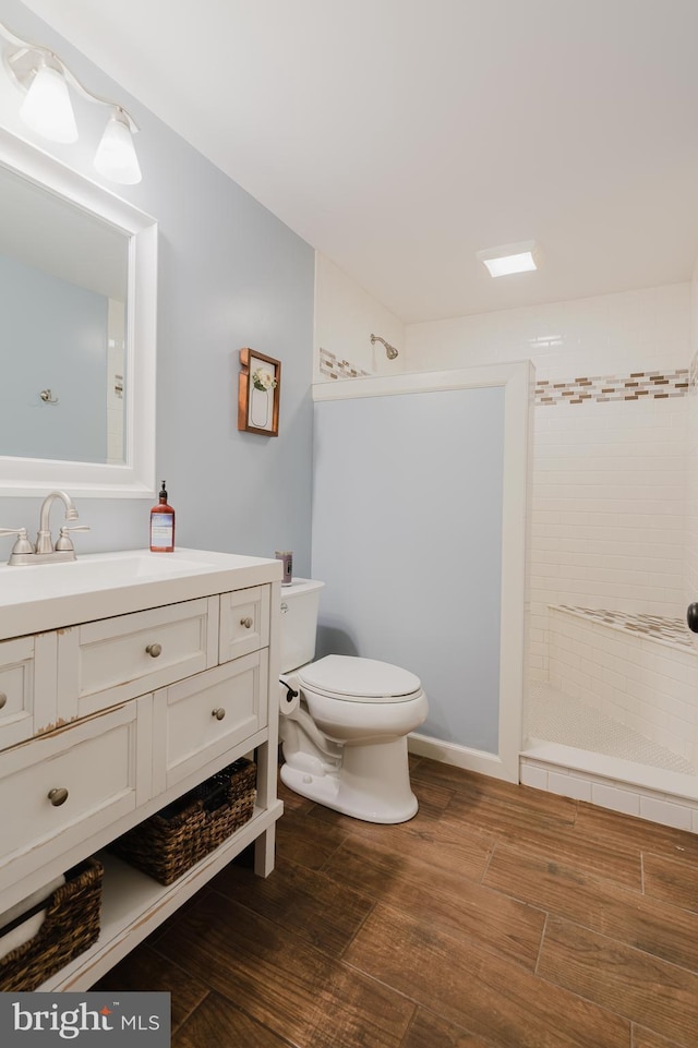 bathroom with vanity, toilet, tiled shower, and wood finished floors