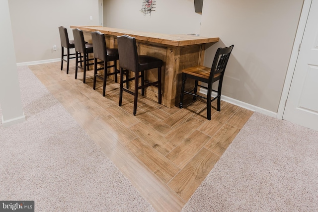 bar with a bar, baseboards, and wood finished floors