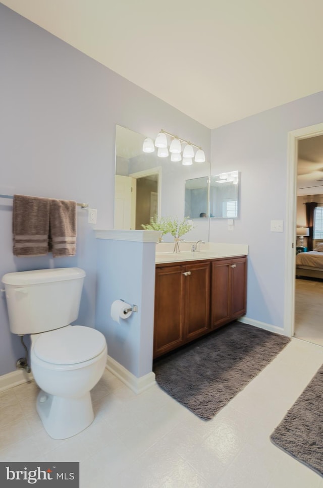ensuite bathroom with connected bathroom, toilet, baseboards, and vanity