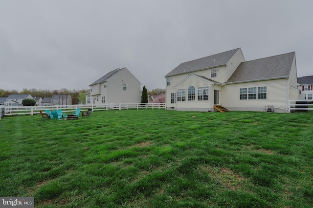 rear view of house with entry steps, a lawn, and a fenced backyard