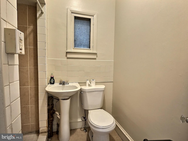 bathroom featuring toilet, tile walls, and a sink