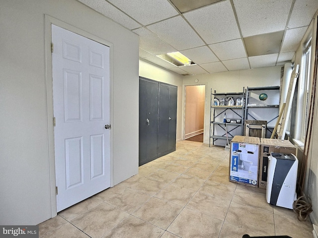 hall with light tile patterned floors and a paneled ceiling