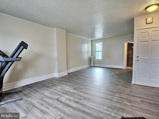 interior space featuring a textured ceiling, ornamental molding, baseboards, and wood finished floors
