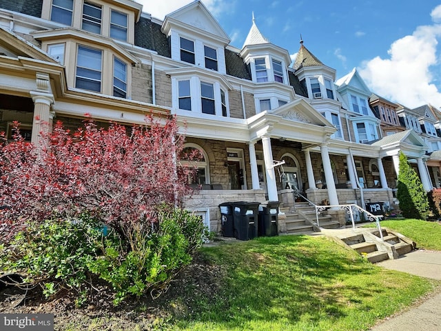 view of front of house with a porch, a front yard, a residential view, mansard roof, and stone siding