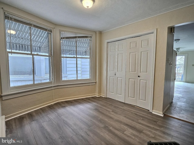 unfurnished bedroom with crown molding, baseboards, dark wood finished floors, and a closet