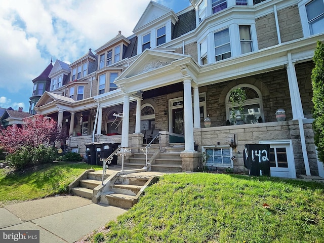 view of property with a porch, mansard roof, and stone siding