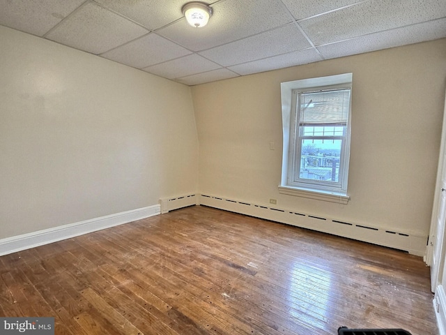 empty room with baseboards, a baseboard radiator, hardwood / wood-style flooring, and a paneled ceiling