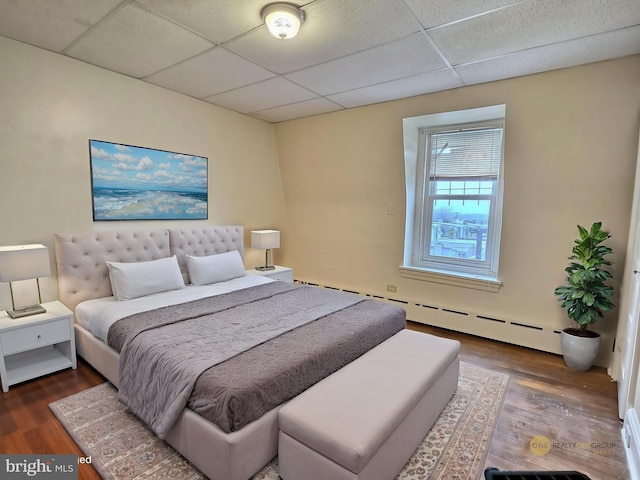 bedroom with wood finished floors, a baseboard heating unit, and a drop ceiling