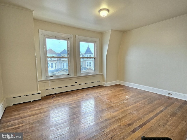 spare room with baseboards, ornamental molding, a baseboard heating unit, and hardwood / wood-style flooring