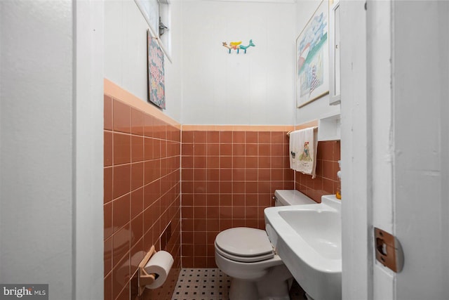half bathroom featuring a sink, tile walls, wainscoting, and toilet