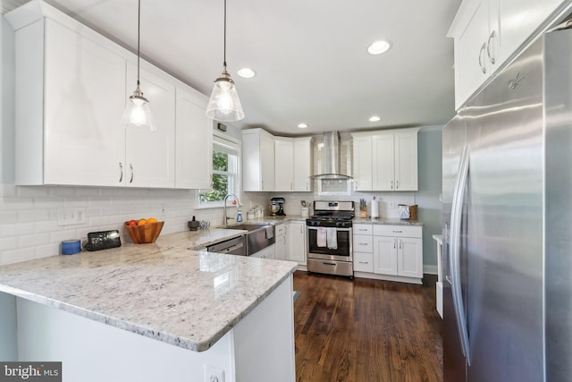 kitchen featuring a peninsula, a sink, wall chimney exhaust hood, stainless steel appliances, and white cabinetry