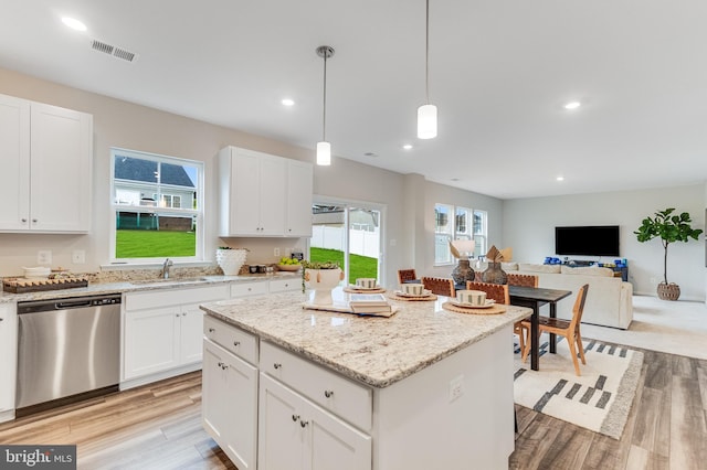 kitchen with stainless steel dishwasher, a kitchen island, open floor plan, a sink, and light wood-style flooring
