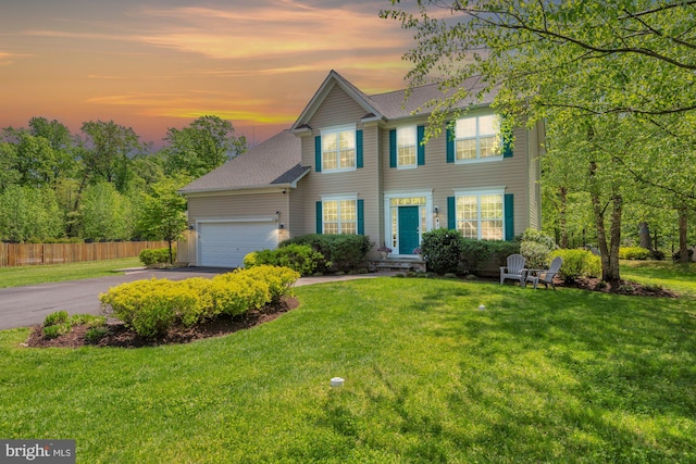 colonial-style house featuring fence, a front yard, a shingled roof, an attached garage, and driveway