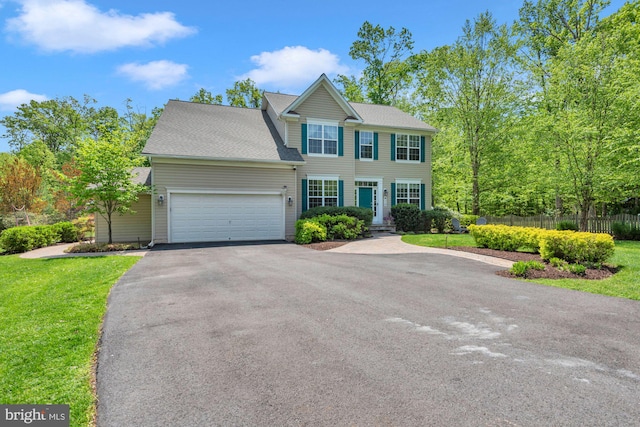 colonial house with an attached garage, fence, driveway, and a front yard