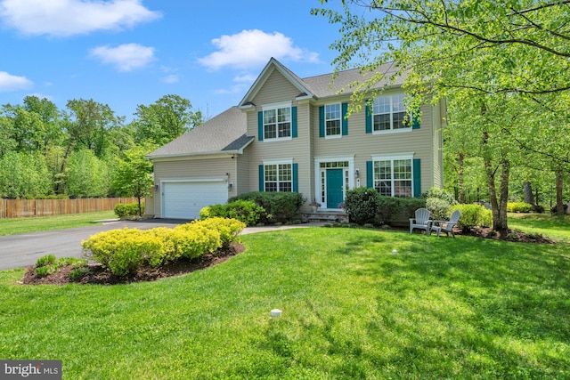 colonial-style house with fence, a shingled roof, an attached garage, a front yard, and driveway