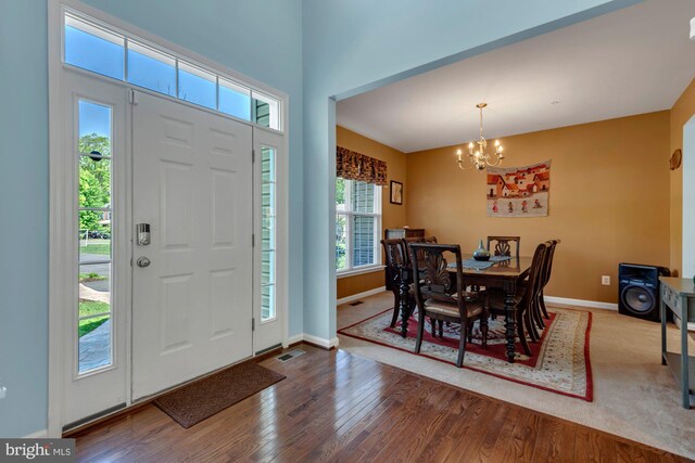 foyer entrance with baseboards, a notable chandelier, wood finished floors, and visible vents