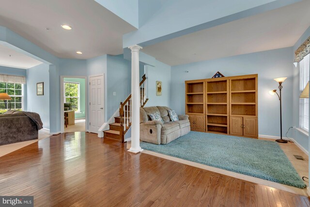 living area featuring visible vents, stairs, wood finished floors, baseboards, and ornate columns