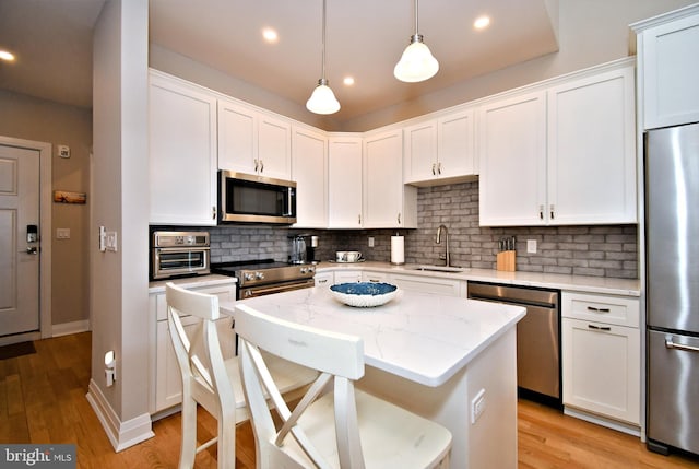 kitchen featuring stainless steel appliances, white cabinetry, a sink, and a center island