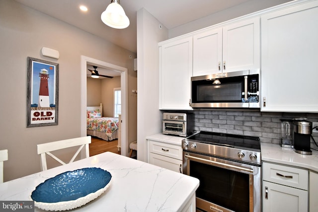 kitchen featuring backsplash, stainless steel appliances, light stone countertops, and white cabinetry