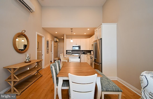 dining room featuring a towering ceiling, light wood-style floors, baseboards, recessed lighting, and a wall unit AC