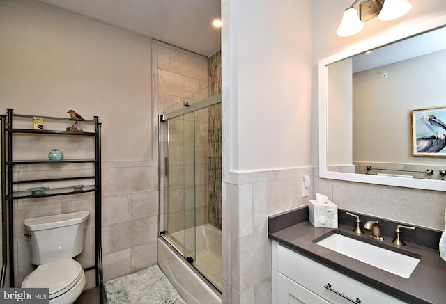 bathroom with wainscoting, vanity, toilet, enclosed tub / shower combo, and tile walls