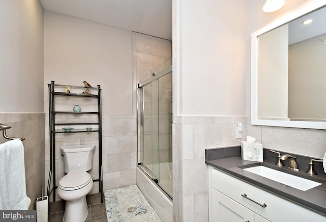 full bathroom with vanity, combined bath / shower with glass door, toilet, and tile walls