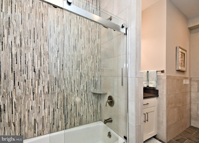 bathroom with wainscoting, shower / bath combination with glass door, and tile walls
