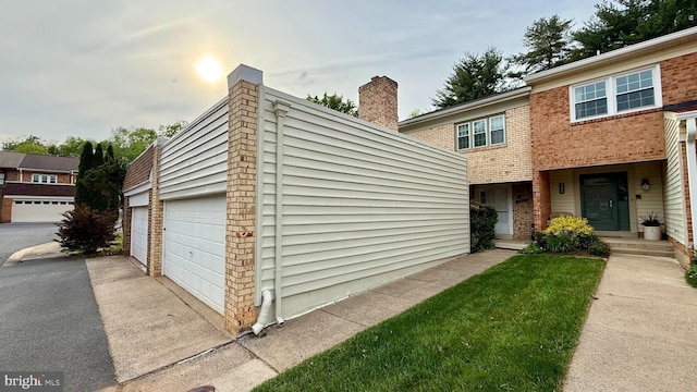 view of front of home featuring brick siding, a garage, an outdoor structure, driveway, and a chimney