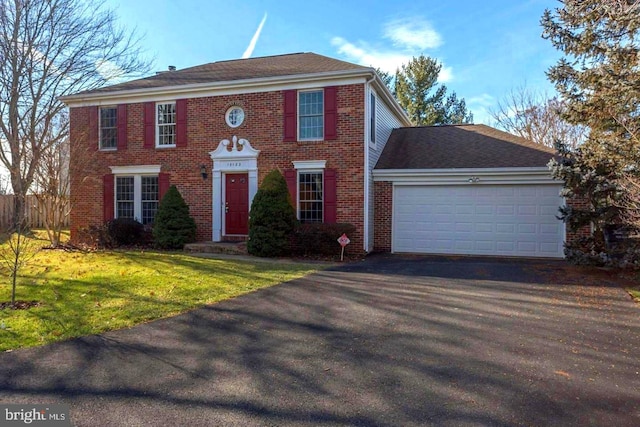 colonial house with brick siding, a garage, a front yard, and aphalt driveway