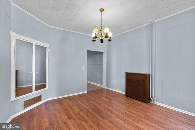 unfurnished dining area featuring an inviting chandelier, baseboards, crown molding, and wood finished floors