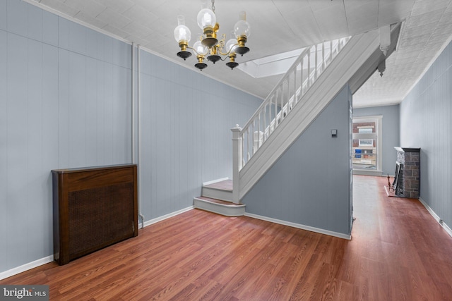 unfurnished dining area with an inviting chandelier, baseboards, wood finished floors, and stairway