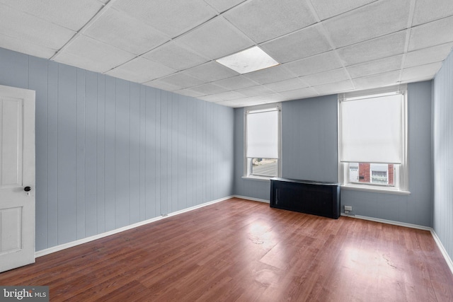 empty room featuring baseboards, a paneled ceiling, wood finished floors, and a wealth of natural light
