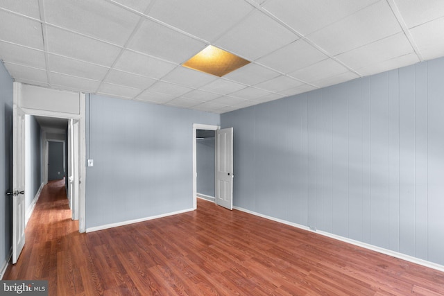 spare room with baseboards, a drop ceiling, and wood finished floors