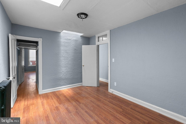 unfurnished bedroom featuring baseboards, radiator, a textured wall, and wood finished floors
