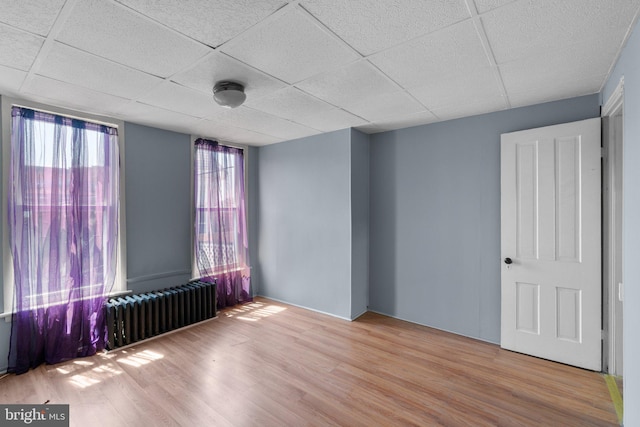 empty room featuring a paneled ceiling, radiator, and wood finished floors
