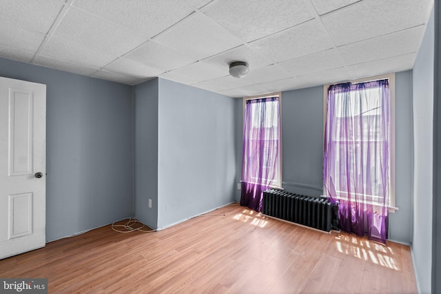 spare room with radiator heating unit, wood finished floors, and a paneled ceiling
