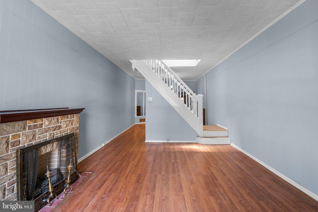 unfurnished living room with stairway, baseboards, a fireplace, and wood finished floors