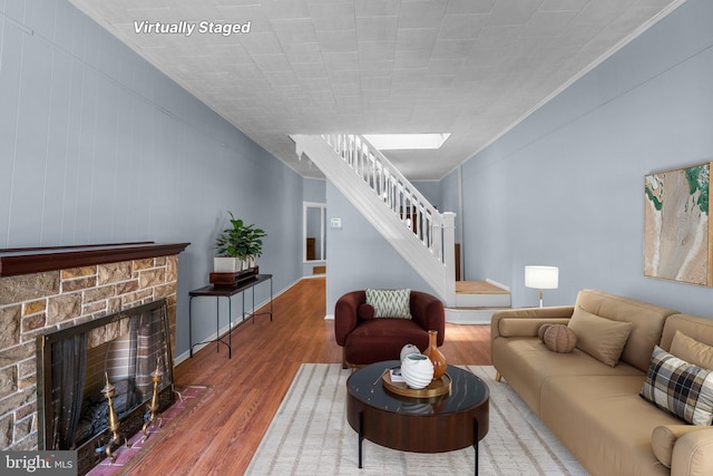 living area with stairway, a skylight, a stone fireplace, and wood finished floors
