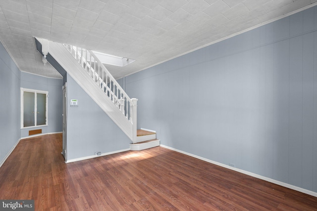 unfurnished living room featuring stairs, baseboards, ornamental molding, and wood finished floors