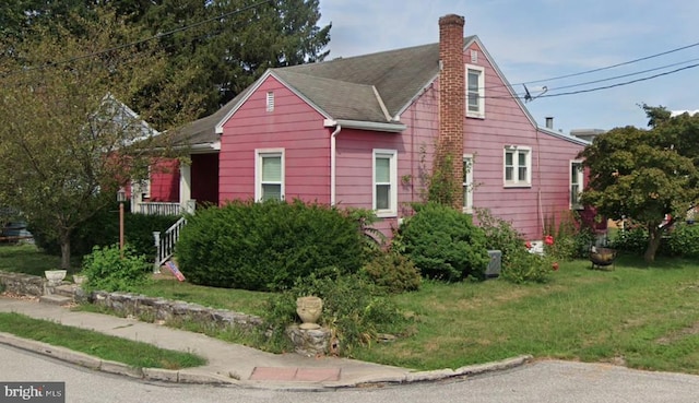 view of front of property featuring a chimney, roof with shingles, and a front lawn