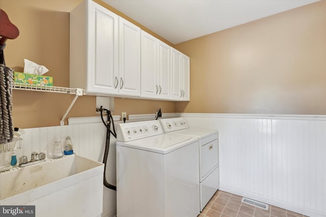 laundry area with visible vents, wainscoting, washing machine and clothes dryer, a sink, and cabinet space