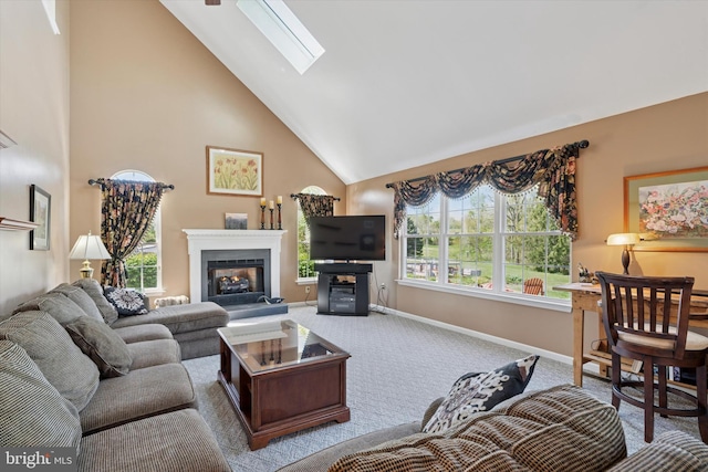 carpeted living room featuring baseboards, a glass covered fireplace, a skylight, and high vaulted ceiling