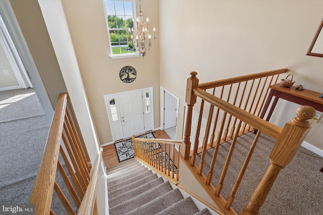 carpeted foyer entrance with baseboards, a notable chandelier, and a towering ceiling