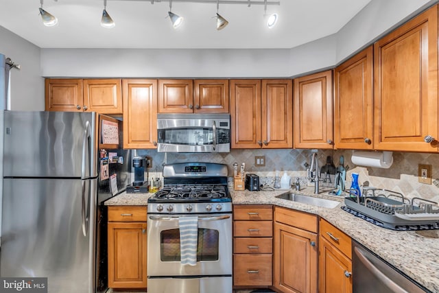 kitchen with brown cabinetry, a sink, decorative backsplash, and stainless steel appliances