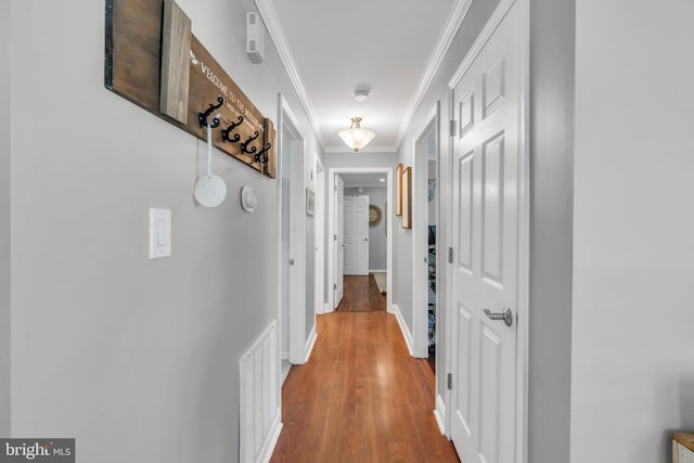 hall with crown molding, baseboards, wood finished floors, and visible vents