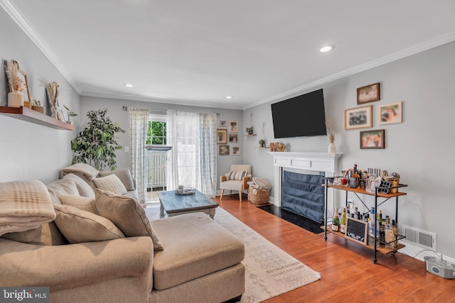living room featuring crown molding, a fireplace with flush hearth, recessed lighting, and wood finished floors