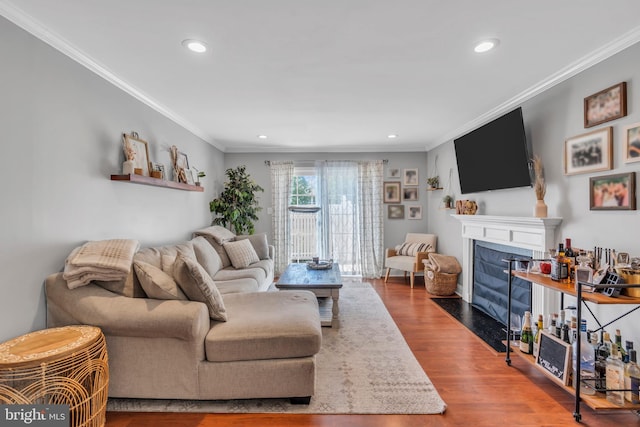 living area featuring crown molding, recessed lighting, a fireplace with flush hearth, and wood finished floors
