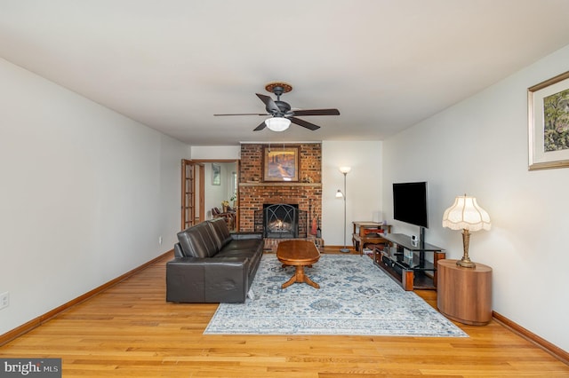 living area featuring baseboards, a fireplace, a ceiling fan, and light wood-type flooring